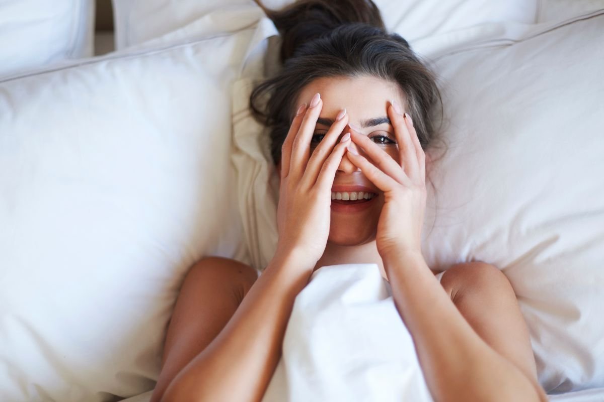 mulher sorrindo na cama cobrindo os olhos 